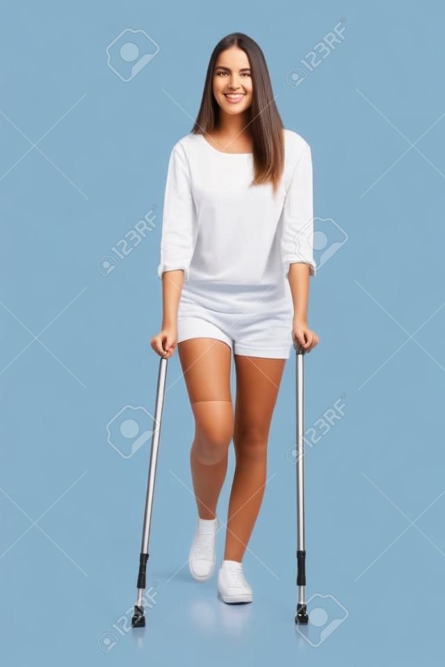 Vista frontal de una mujer caminando con muletas aislados en un fondo blanco