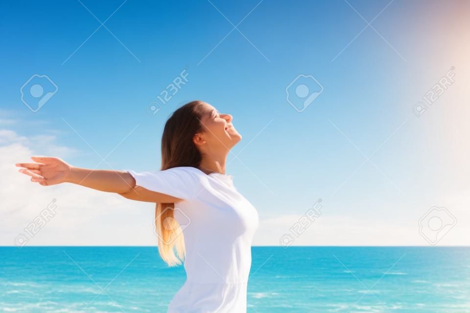 행복 편안한 여자가 깊은 신선한 공기를 호흡​​하고 백그라운드에서 수평선과 해변에 팔을 제기