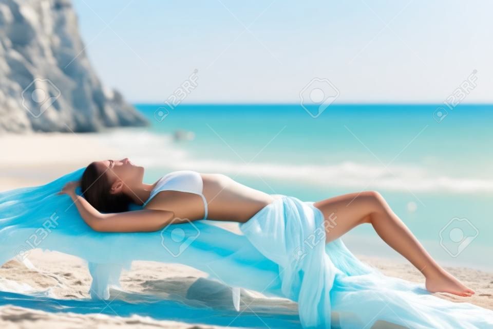 Sunbather belle femme de bronzage sur la plage avec la mer en arrière-plan