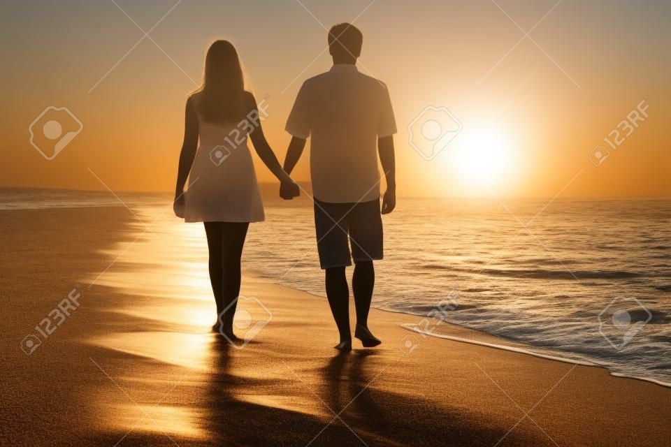 ウォーキングや、夕暮れ時のビーチの砂の上手を繋いでいるカップルの背面図