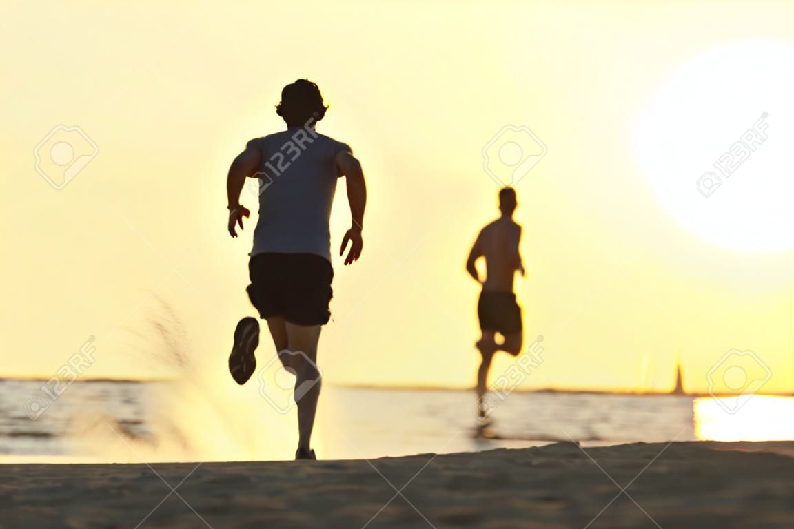 バック グラウンドで太陽と夕日、ビーチで走っているランナー人の背面図シルエット