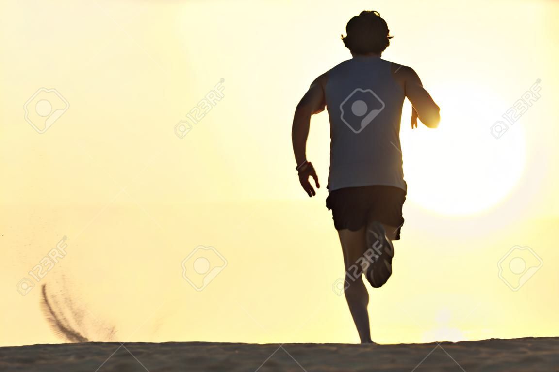Achteraanzicht silhouet van een renner die op het strand loopt bij zonsondergang met zon op de achtergrond