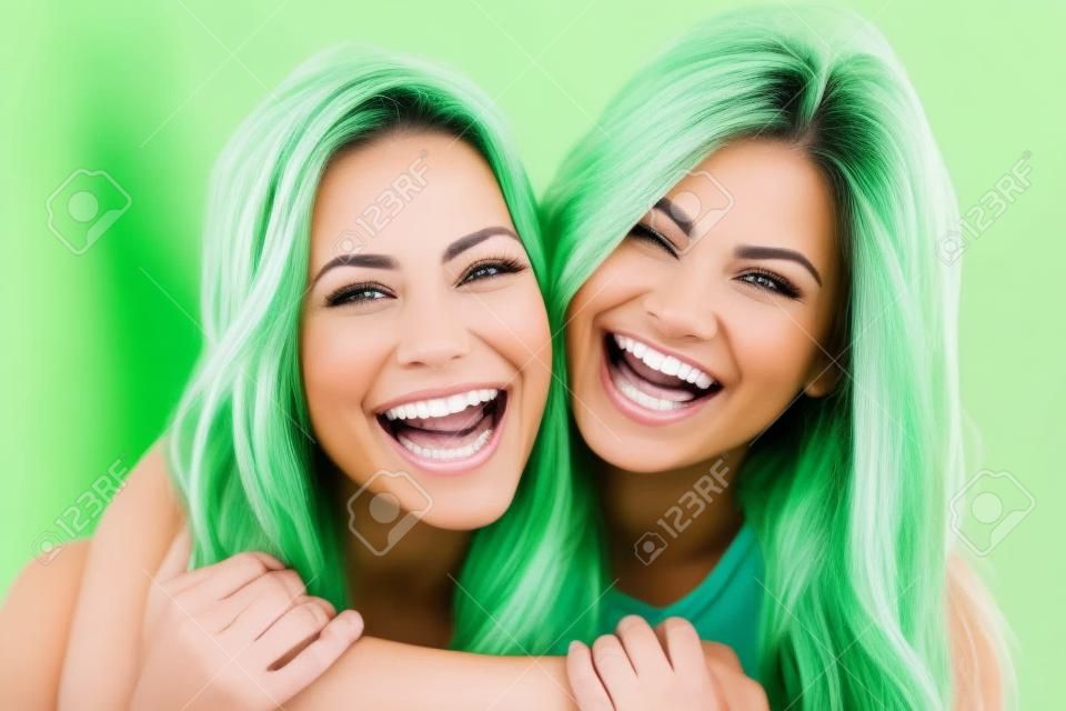 Zwei Freundinnen mit einem perfekten weißen Zähne lachend mit einem grünen Hintergrund