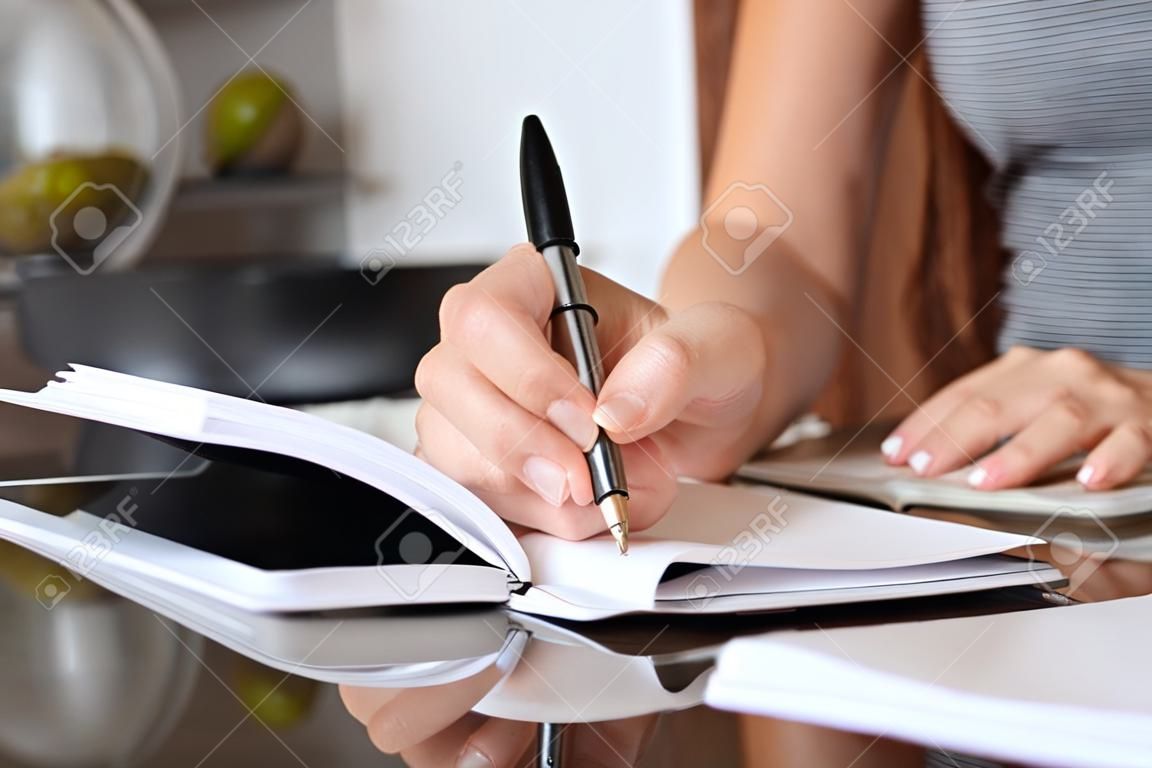 Close up of a woman writer hand writing in a notebook at home in the kitchen