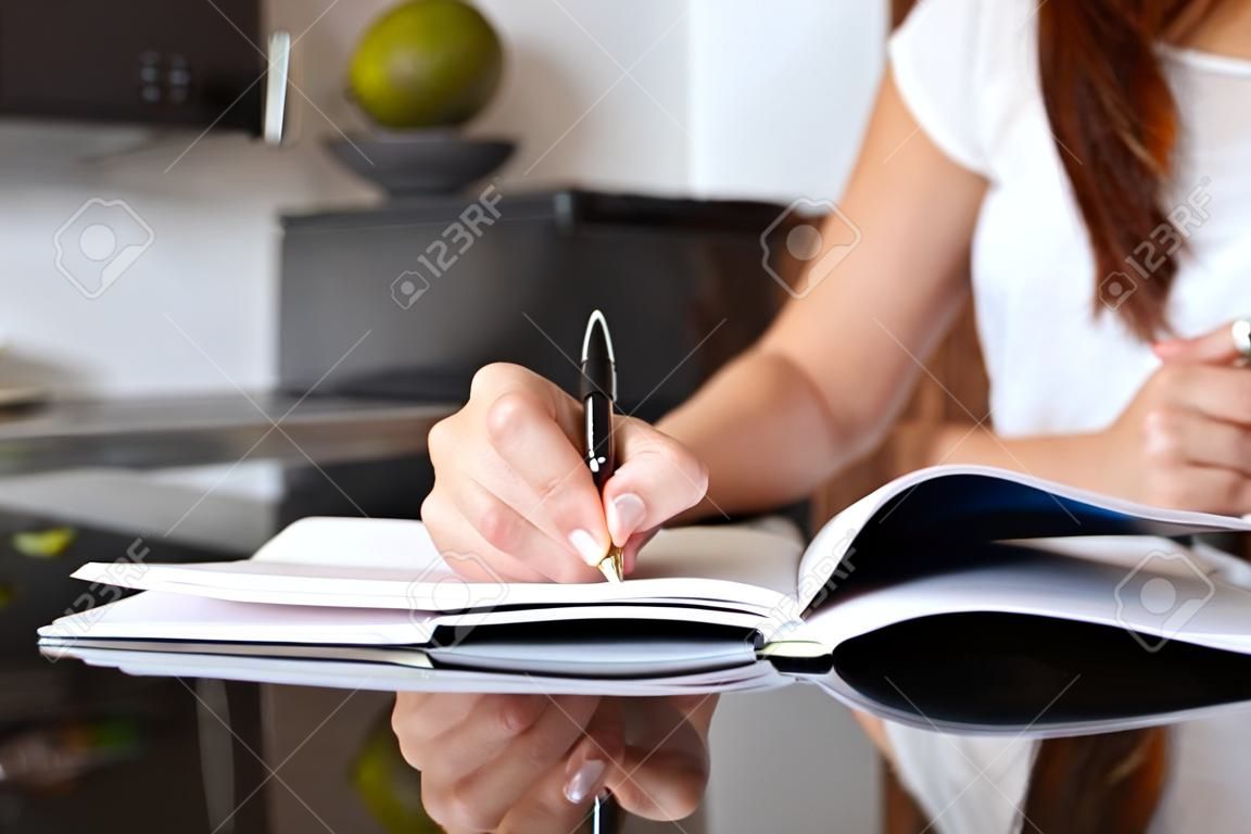 Közelről egy írónő kézzel írás egy notebook otthon a konyhában