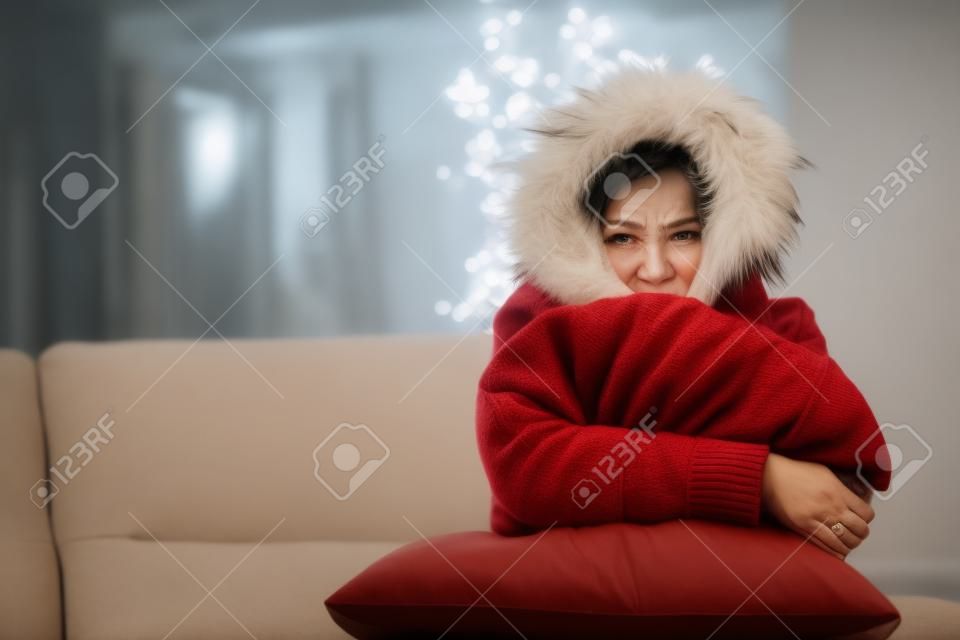 소파에 앉아 따뜻하게 추운 집에서 옷을 입고 화가 여자