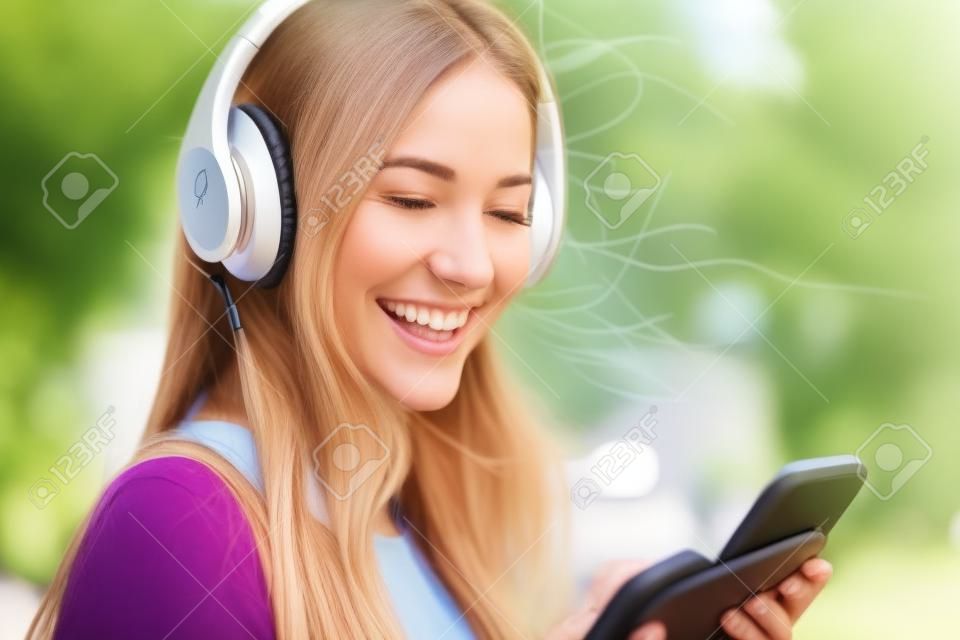 Portrait eines glücklichen Mädchens auf Linie mit drahtlosen Kopfhörer von einem Smartphone auf der Straße in einem sonnigen Tag im Sommer hören Musik