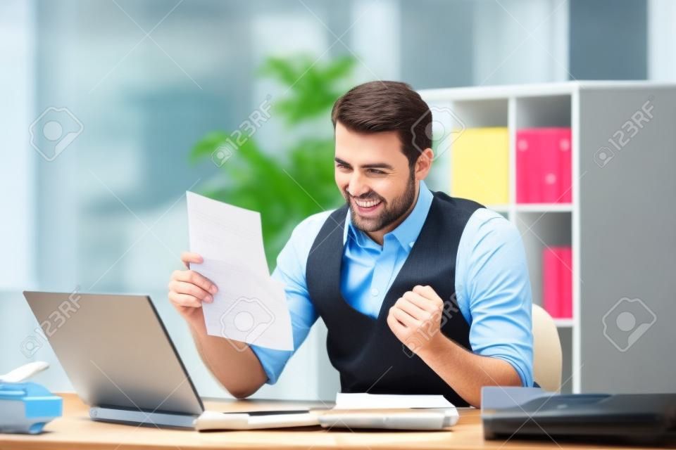 Возбужденные бизнесмен читает хорошие новости в письме аа в рабочем столе в офисе