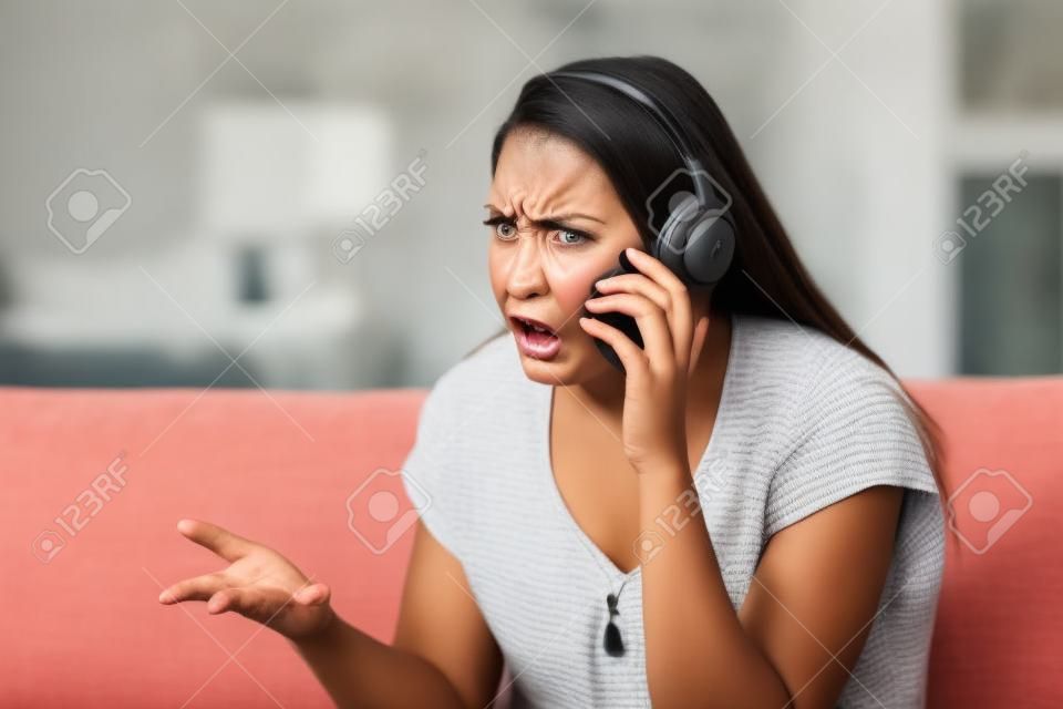 Angry woman arguing during a phone call sitting on a couch in the living room at home