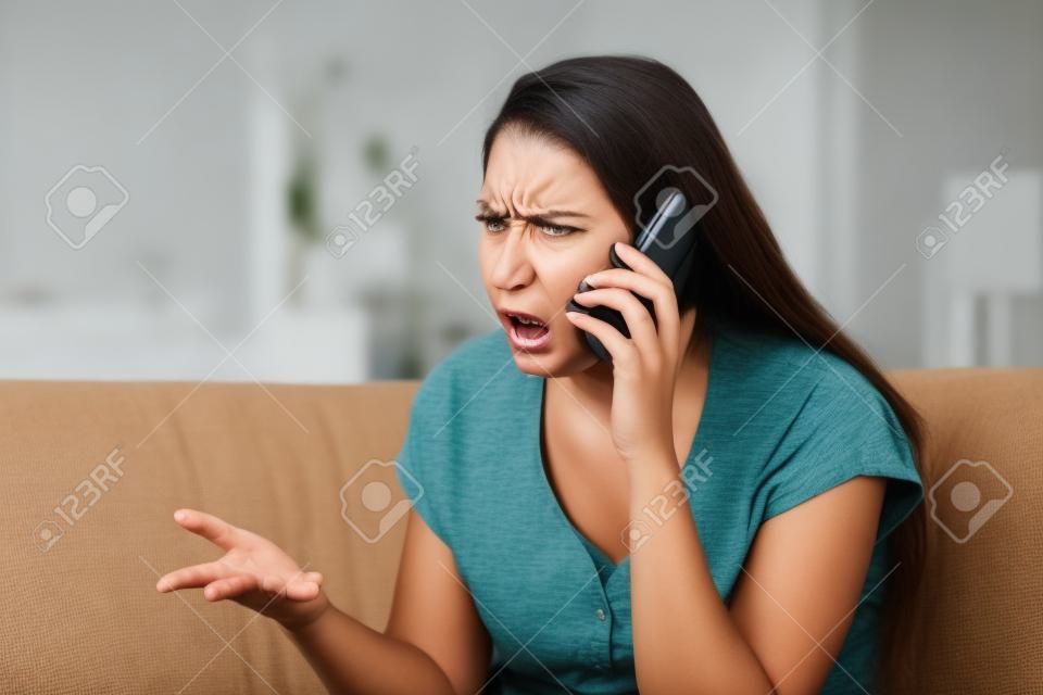 Angry kobieta argumentując podczas rozmowy telefonicznej siedzi na kanapie w salonie w domu
