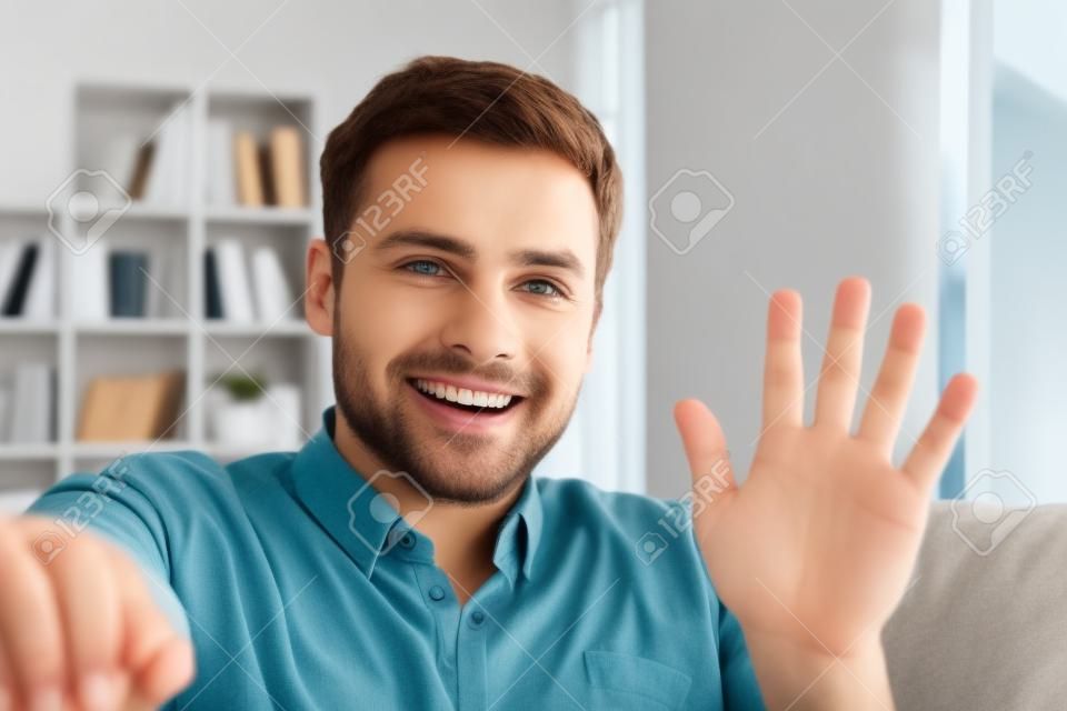 Man waving on a video call sitting on a sofa at home