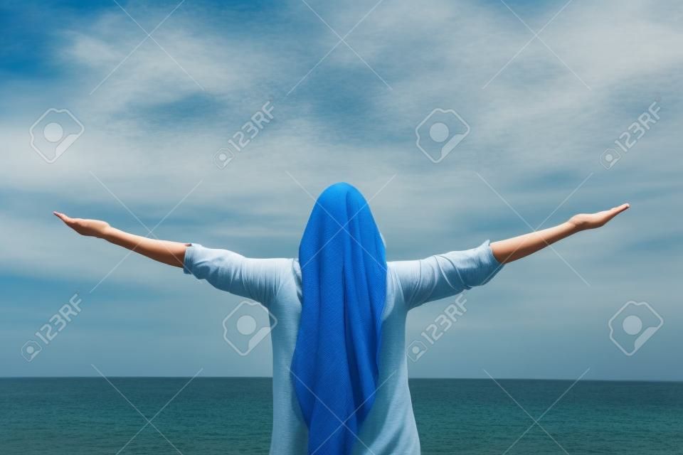 Back view portrait of a woman outstretching arms outdoors to the sea and sky