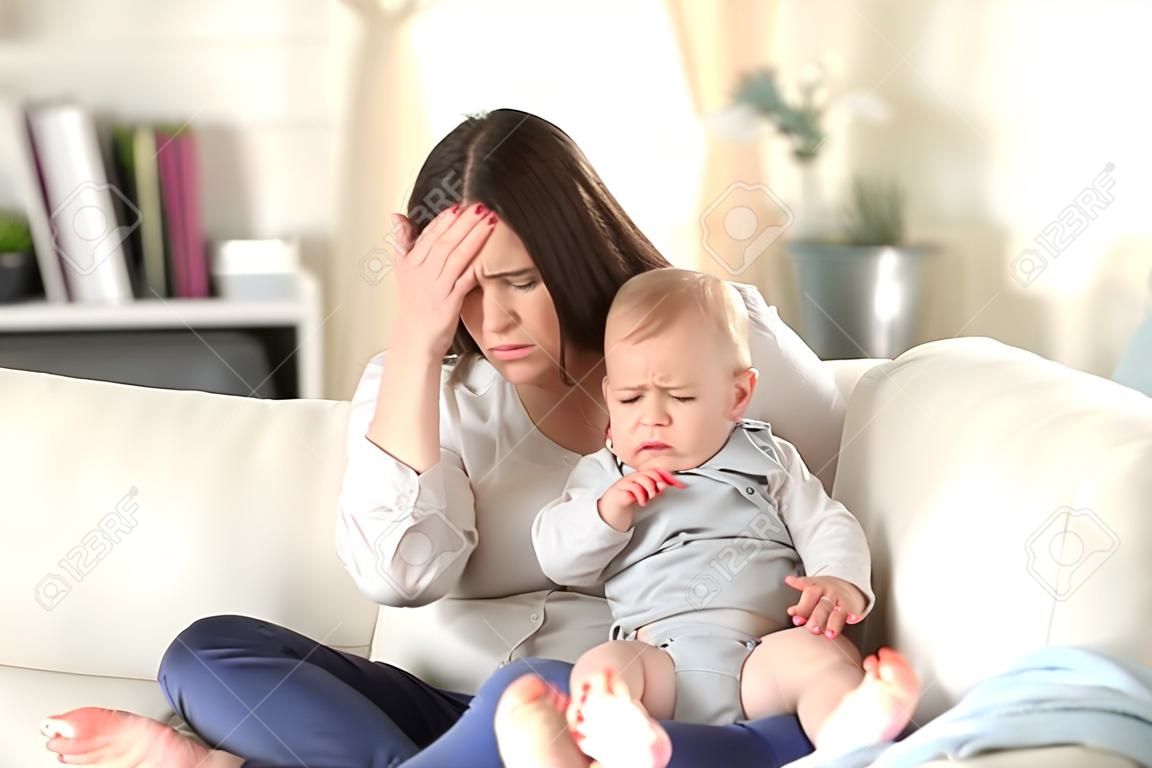 Acı çeken anne ve çaresizce evde oturma odasında bir kanepede oturan ağlayan bebek