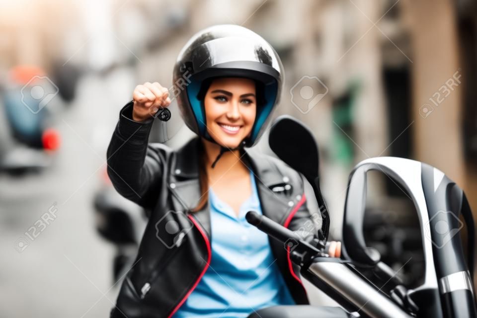 Satisfied biker showing motorbike keys on her scooter on the street