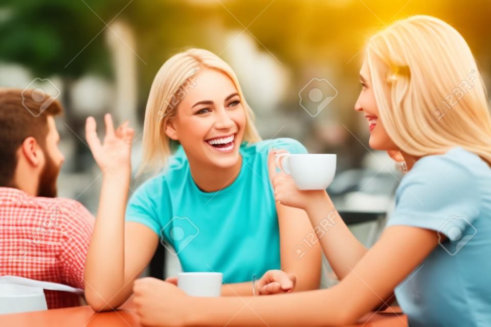 Due amici felici che parlano e bevono in una terrazza di una caffetteria