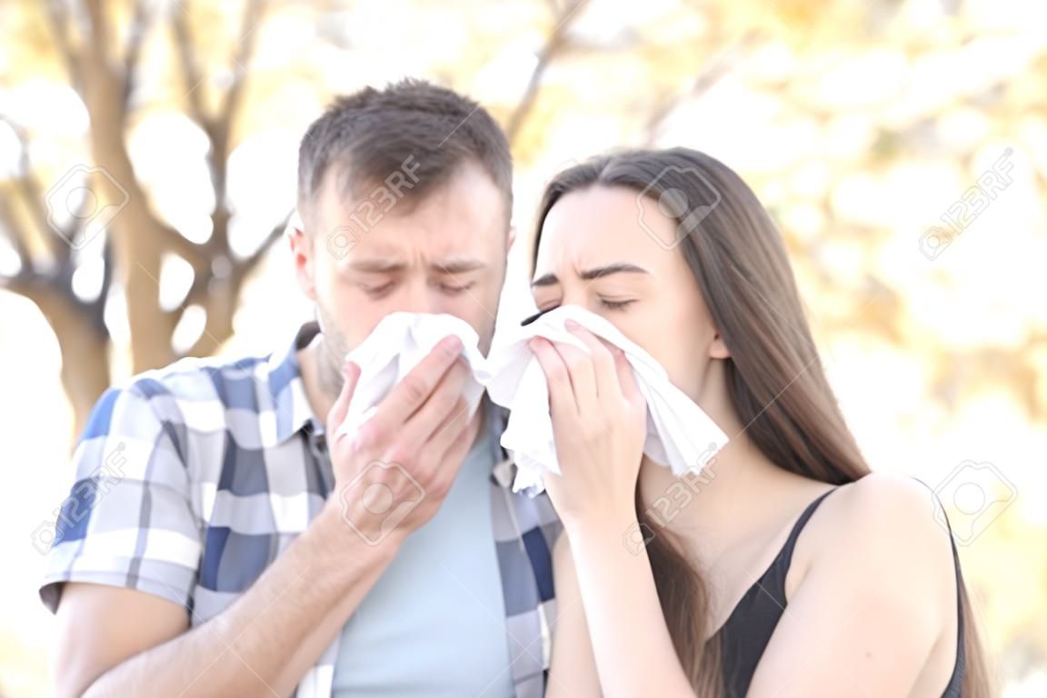 Sick couple sneezing together covering mouth with wipes in a park
