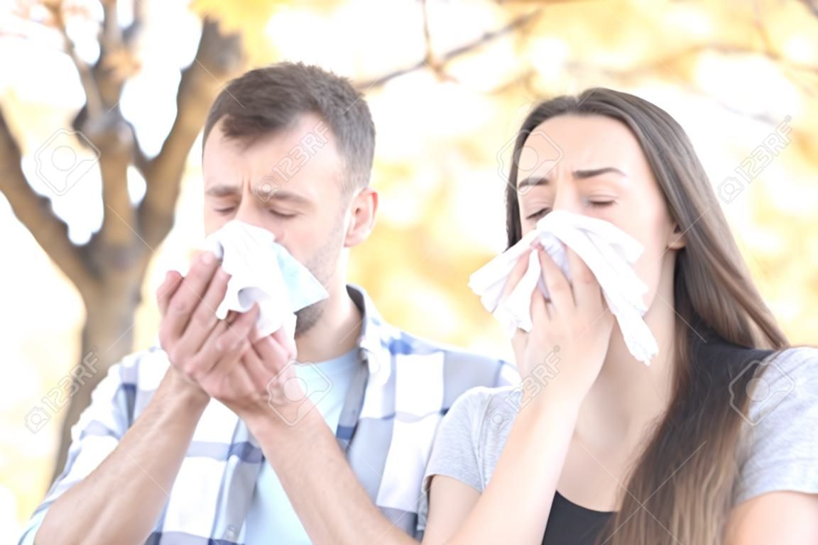 Sick couple sneezing together covering mouth with wipes in a park