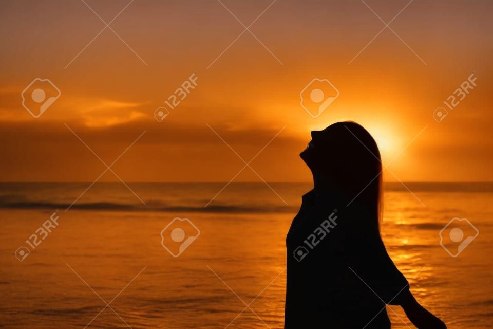 Seitenansichtporträt einer glücklichen Frauensilhouette am Strand, die bei Sonnenuntergang atmet