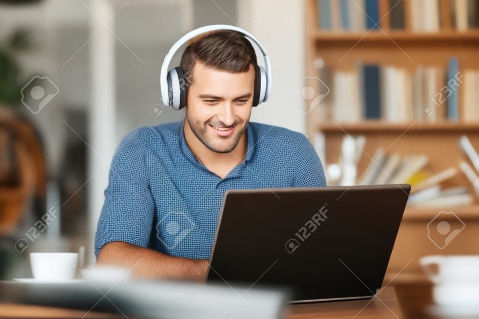 Adult man wearing headphones using a laptop e-learning in a coffee shop or home