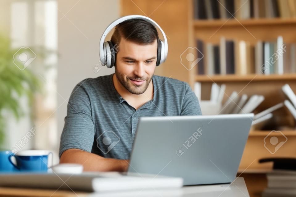 Uomo adulto che indossa le cuffie utilizzando un computer portatile e-learning in una caffetteria o a casa