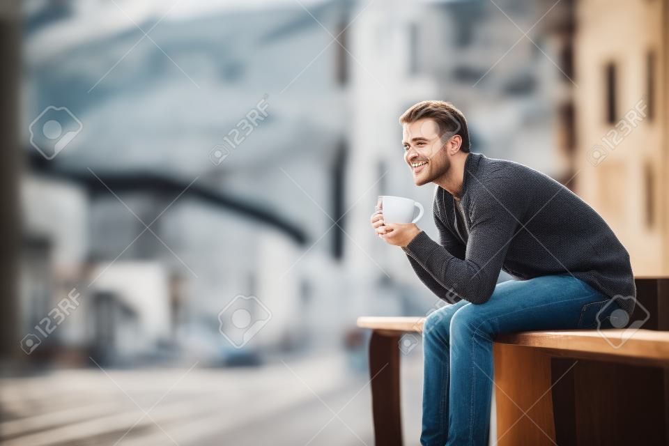 Happy man koffie drinken overwegend uitzicht zittend op een balkon buiten in een kuststad