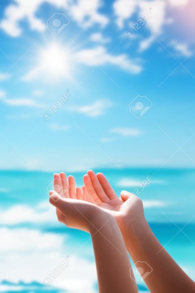 Руки женщины кладут вместе, как молятся на фоне океана природы и голубого неба.