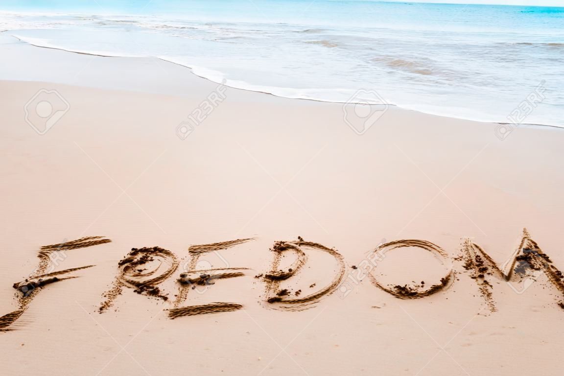 Freedom word hand drawn on sand summer beach background.