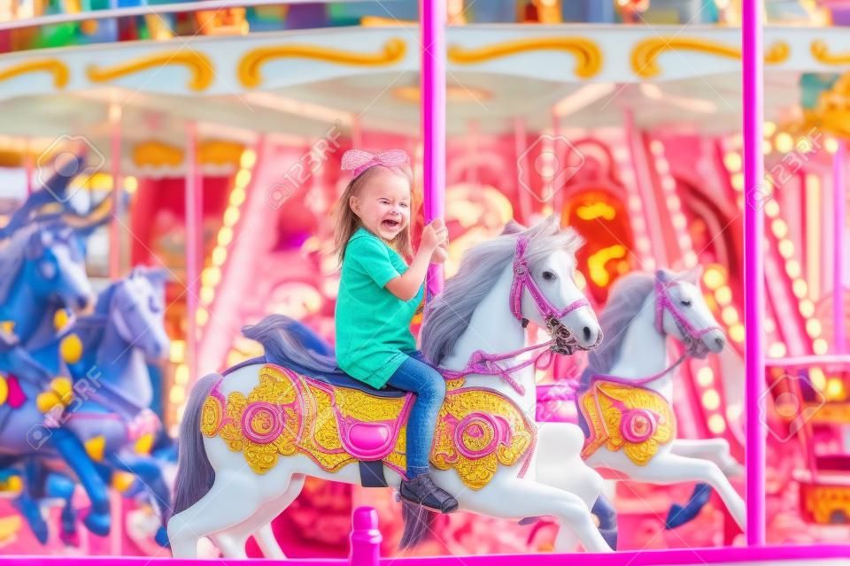 Szczęśliwa dziewczynka jeździ latem na karuzeli na koniu w parku rozrywki