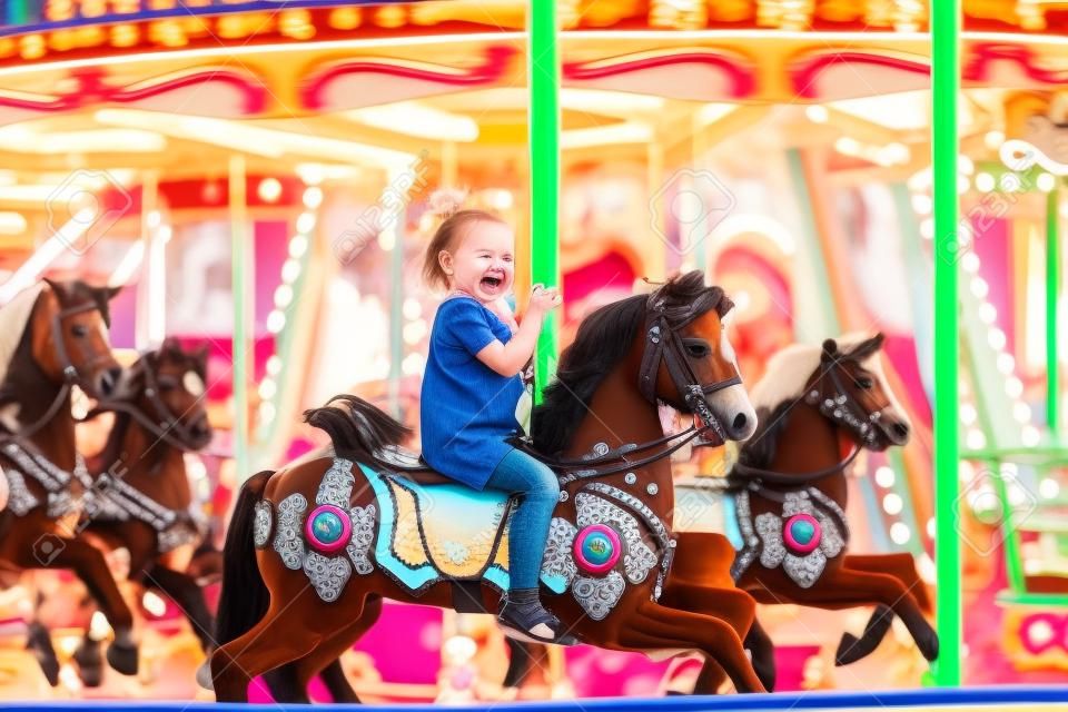 Szczęśliwa dziewczynka jeździ latem na karuzeli na koniu w parku rozrywki
