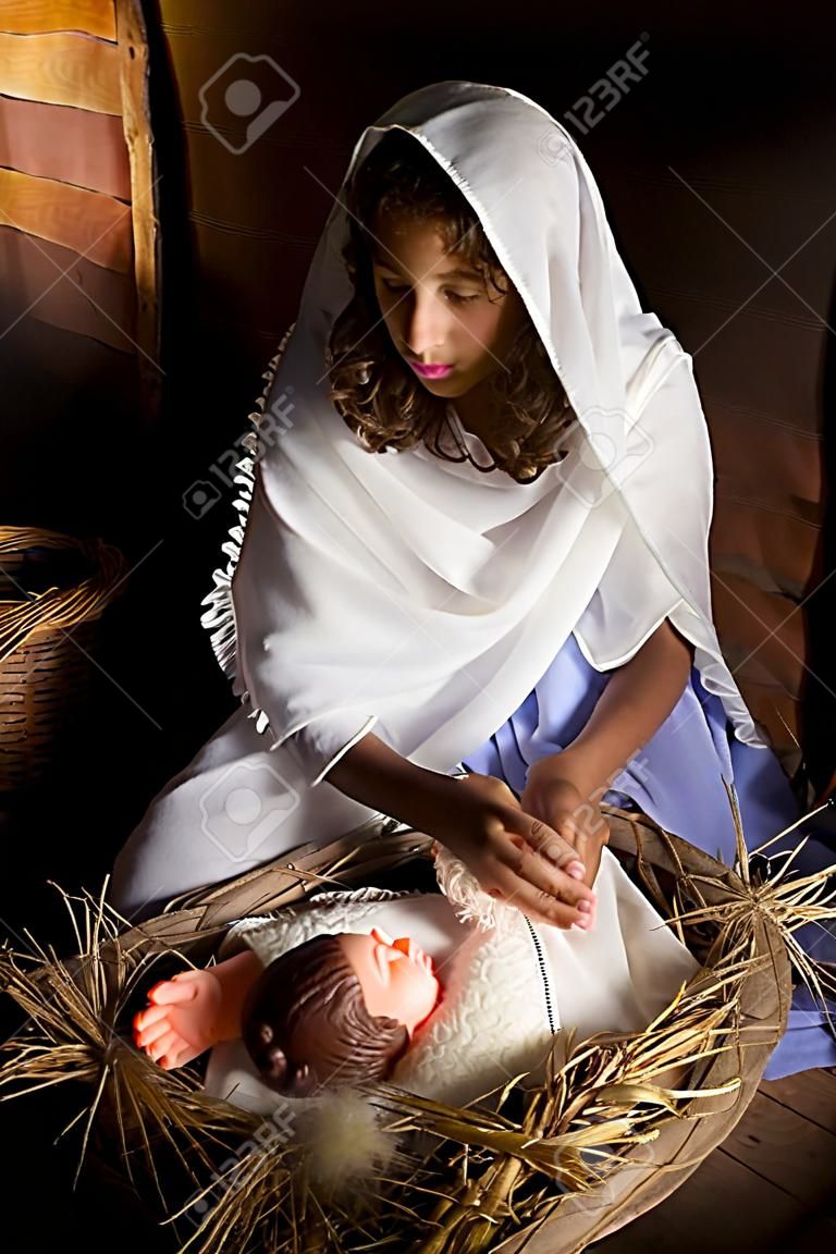 Giovane ragazza giocando il ruolo della Vergine Maria con una bambola in una scena dal vivo presepe di Natale