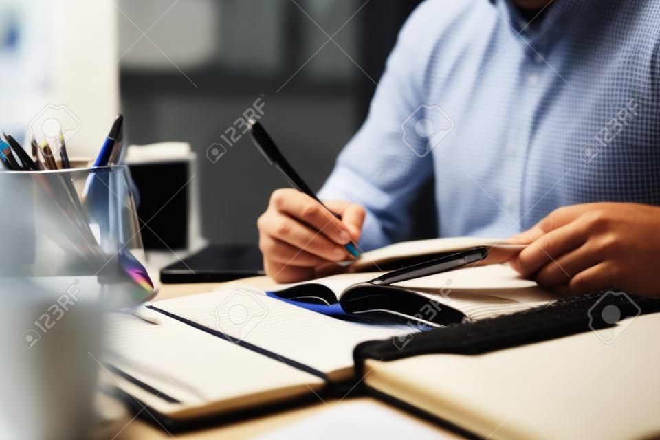 Las manos del hombre con un bolígrafo escribiendo en un cuaderno en la oficina aprendiendo educación y trabajo escribe objetivos, planes para hacer y una lista de deseos en el escritorio