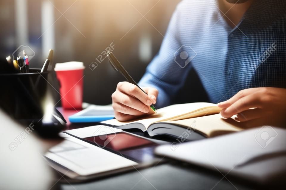 Ręce mężczyzny za pomocą pióra piszącego na notatniku w biurze, ucząc się, edukacji i pracy, zapisują cele, plany do zrobienia i listę życzeń na biurku