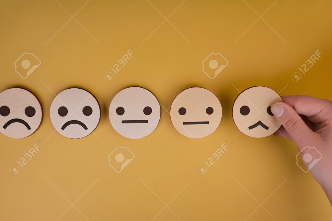 El círculo de bloques de madera de mano elige conceptos de evaluación de servicio al cliente y encuesta de satisfacción de cara de sonrisa de icono en el espacio de copia de fondo amarillo