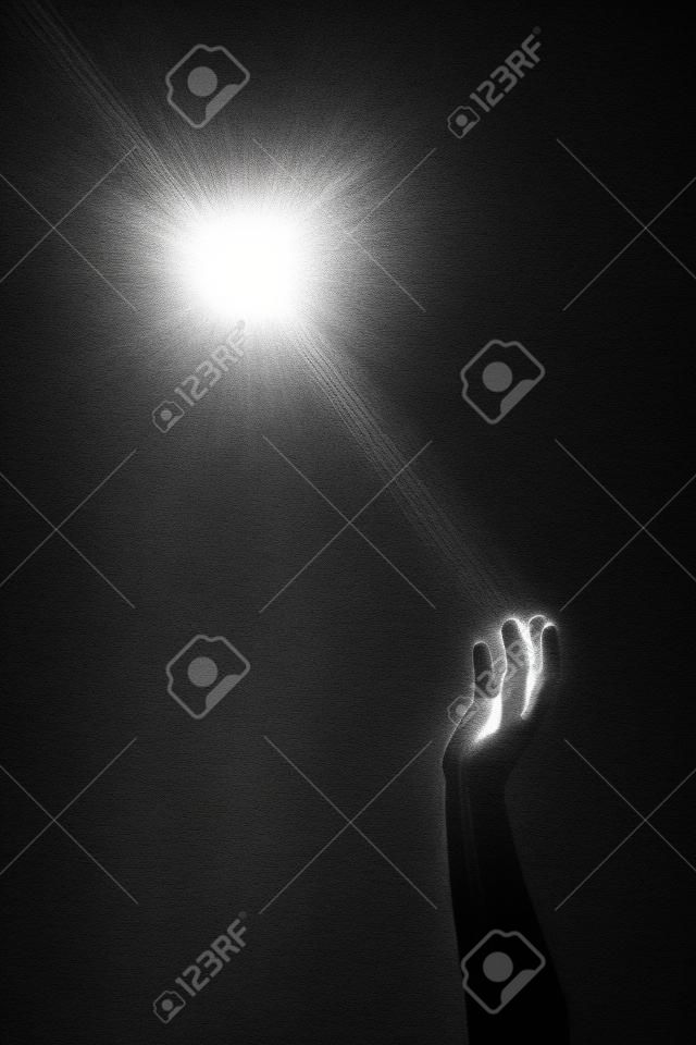 Foto monocromatica concettuale artistica di una mano che raggiunge un raggio di luce