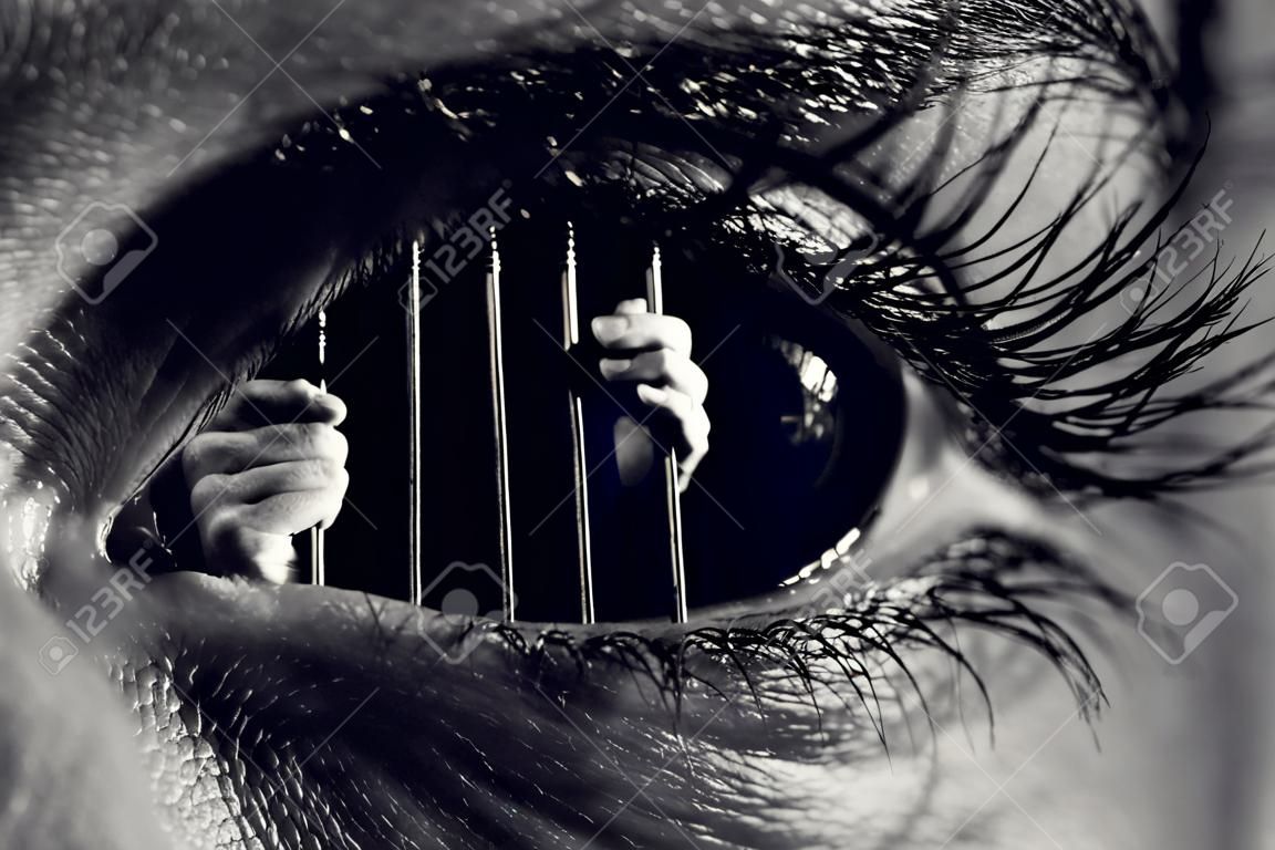 Fotografía monocromática conceptual de manos sosteniendo los barrotes de una prisión dentro de un ojo humano