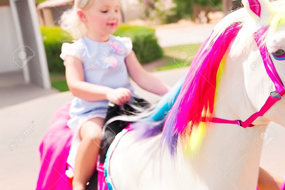 Little girl riding a unicorn at the little girl birthday party.