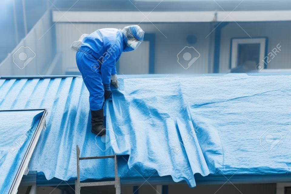 Remoção profissional de amianto. Os homens em ternos de proteção estão removendo as coberturas onduladas de cimento de amianto