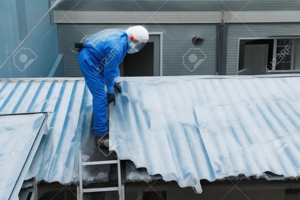 Rimozione amianto professionale. Uomini in tute protettive stanno rimuovendo il tetto ondulato in cemento amianto