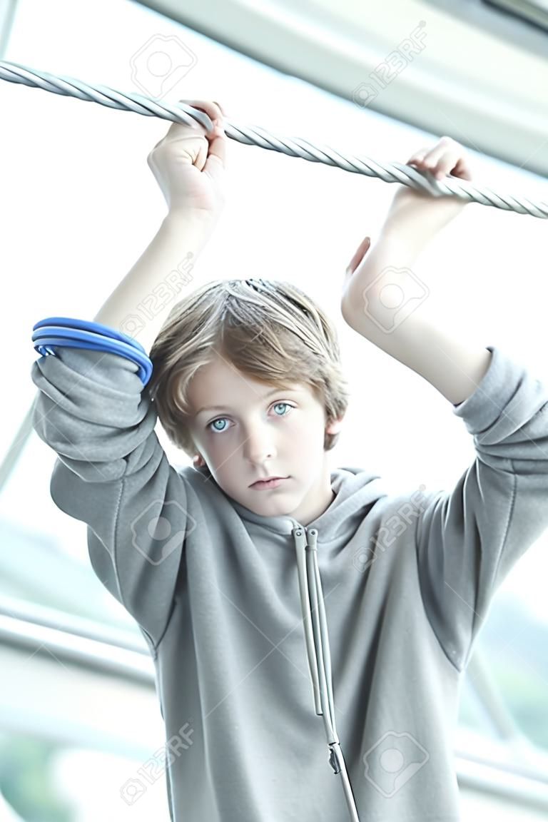 portrait d'un adolescent mâle rêveur tenant un câble métallique à deux mains.