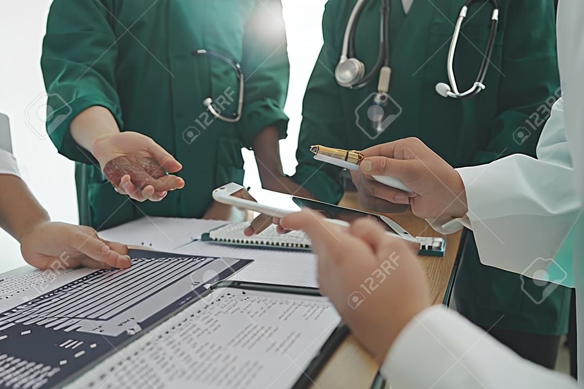 Équipe multiraciale de médecins discutant d'un patient debout regroupé dans le hall regardant une tablette informatique vue rapprochée