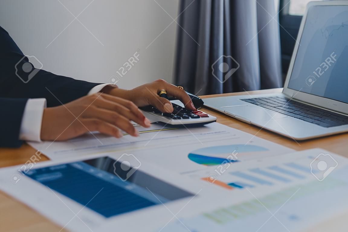Nahaufnahme einer Geschäftsfrau, die Taschenrechner und Laptop für mathematische Finanzen auf einem Holztisch nutzt, Steuerbuchhaltungsstatistiken und analytisches Forschungskonzept