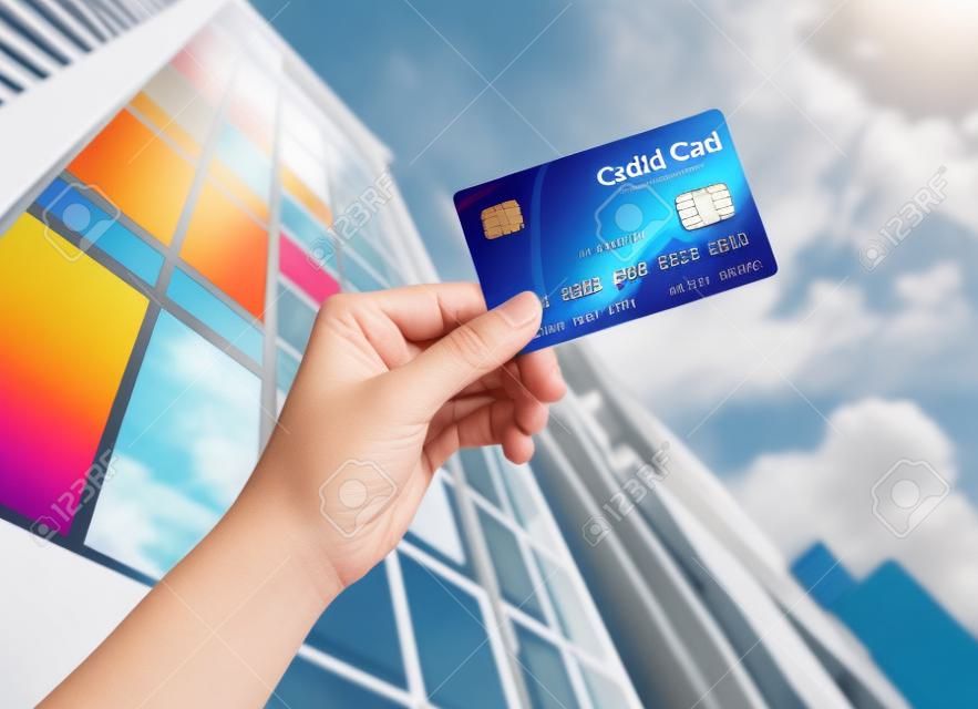 hand holding credit card against builind and sky