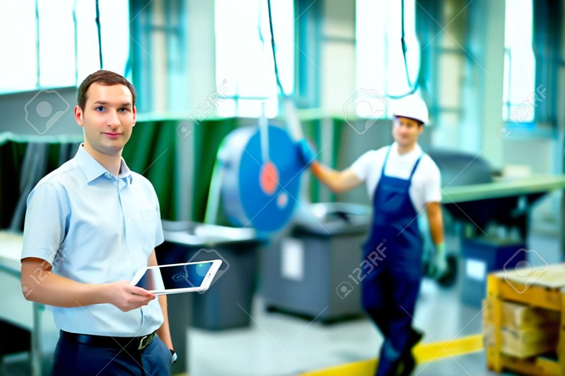 giovane sporgenza con l'operaio in background nella sua fabbrica