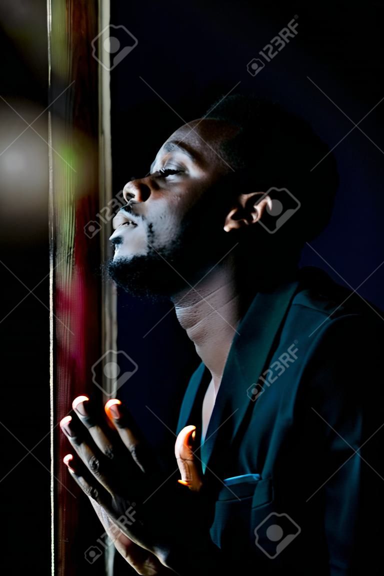 Uomo africano che prega per Dio nella stanza buia. Stile basso