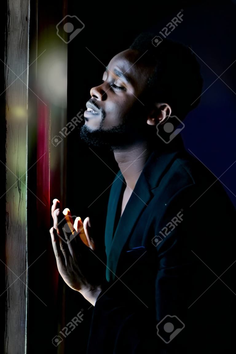 Homem africano orando por Deus no quarto escuro.Low key style