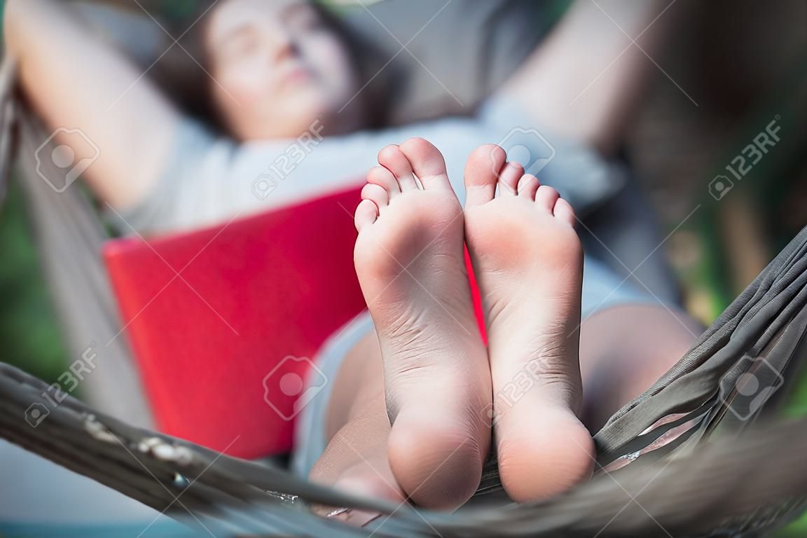 Schläfrige Frau entspannt sich in einer Hängematte, nachdem sie online gearbeitet hat, mit einem Laptop auf ihr. Konzept der Entspannung in der Natur und Nutzung von Technologie