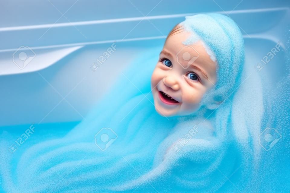 Niña que se divierte en una bañera llena de espuma de jabón.