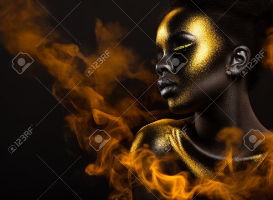 年轻黑人妇女与银和黄金化妆和身体艺术的黑色背景与烟雾