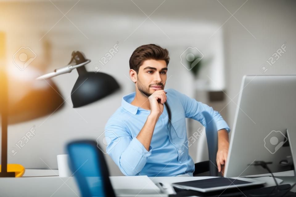 Młody mężczyzna pracuje na komputerze, siedząc w swoim miejscu pracy w biurze