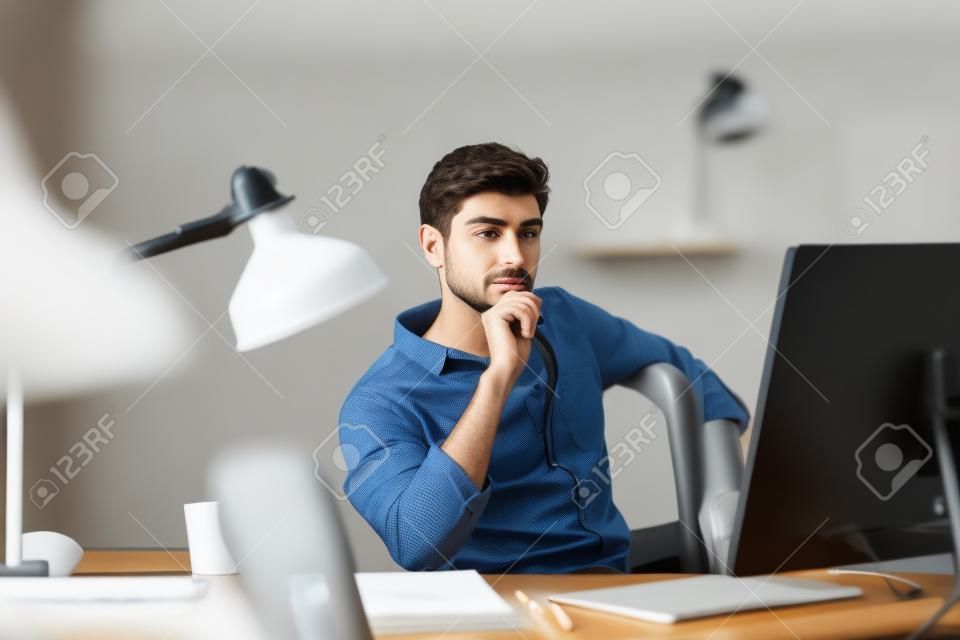 Młody mężczyzna pracuje na komputerze, siedząc w swoim miejscu pracy w biurze